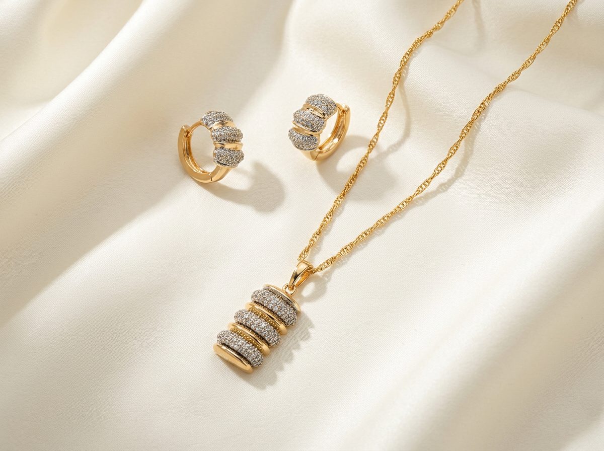 Bin Maqsood gold-tone cylinder pave pendant necklace with matching earrings on ivory silk.